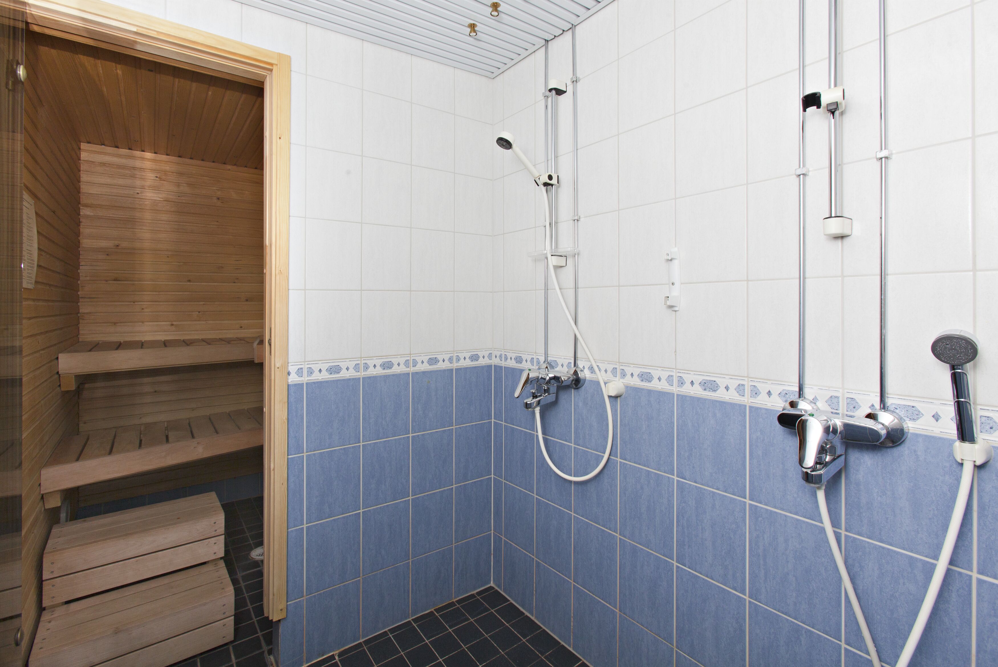 Een badkamer met een houten sauna bank, een douche met een handdouche en een muurbevestigde kraan.