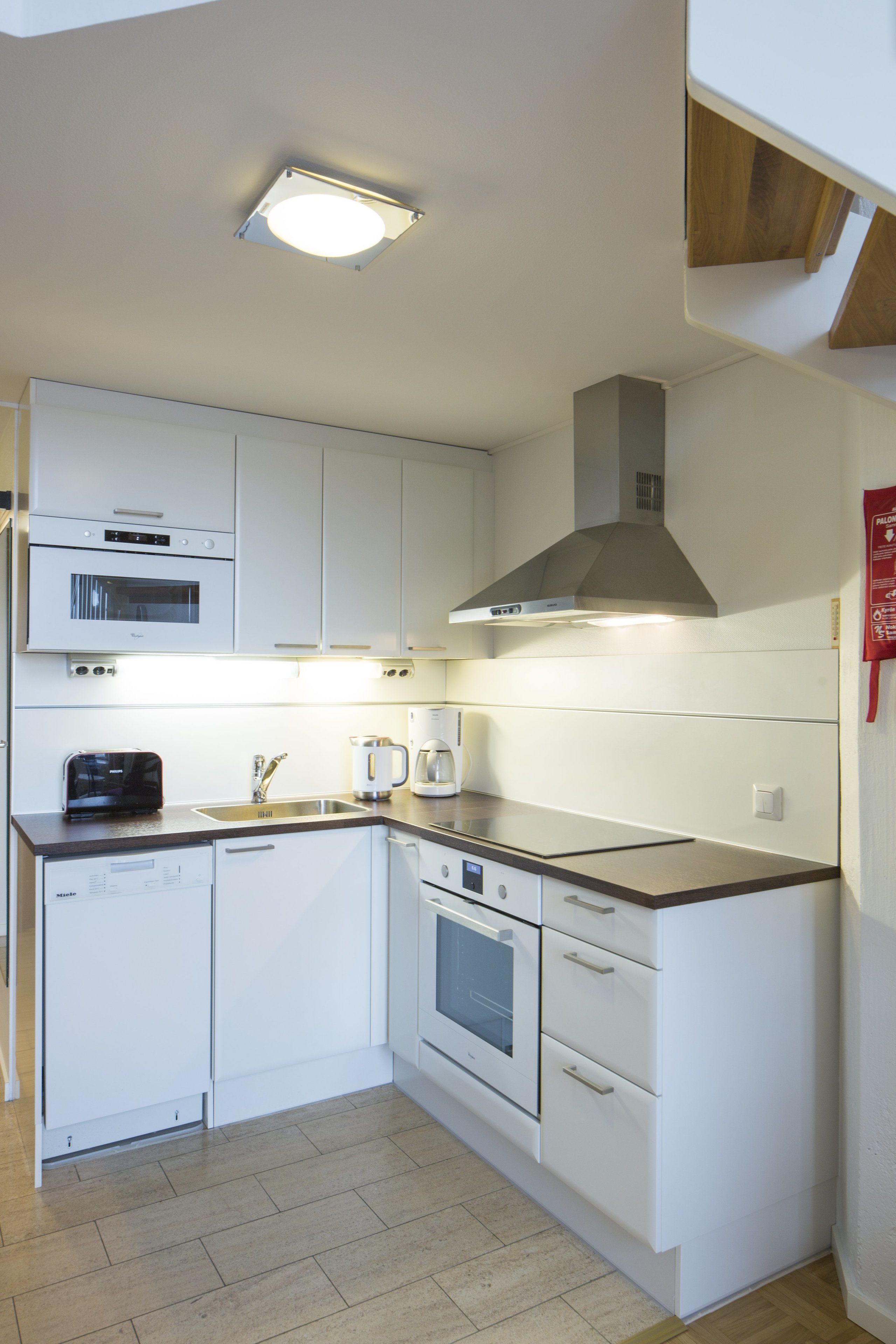 Una cocina moderna con armarios blancos, horno empotrado, microondas y cafetera.