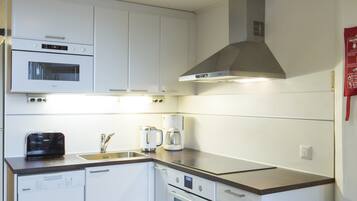 Una cocina moderna con armarios blancos, horno empotrado, microondas y cafetera.