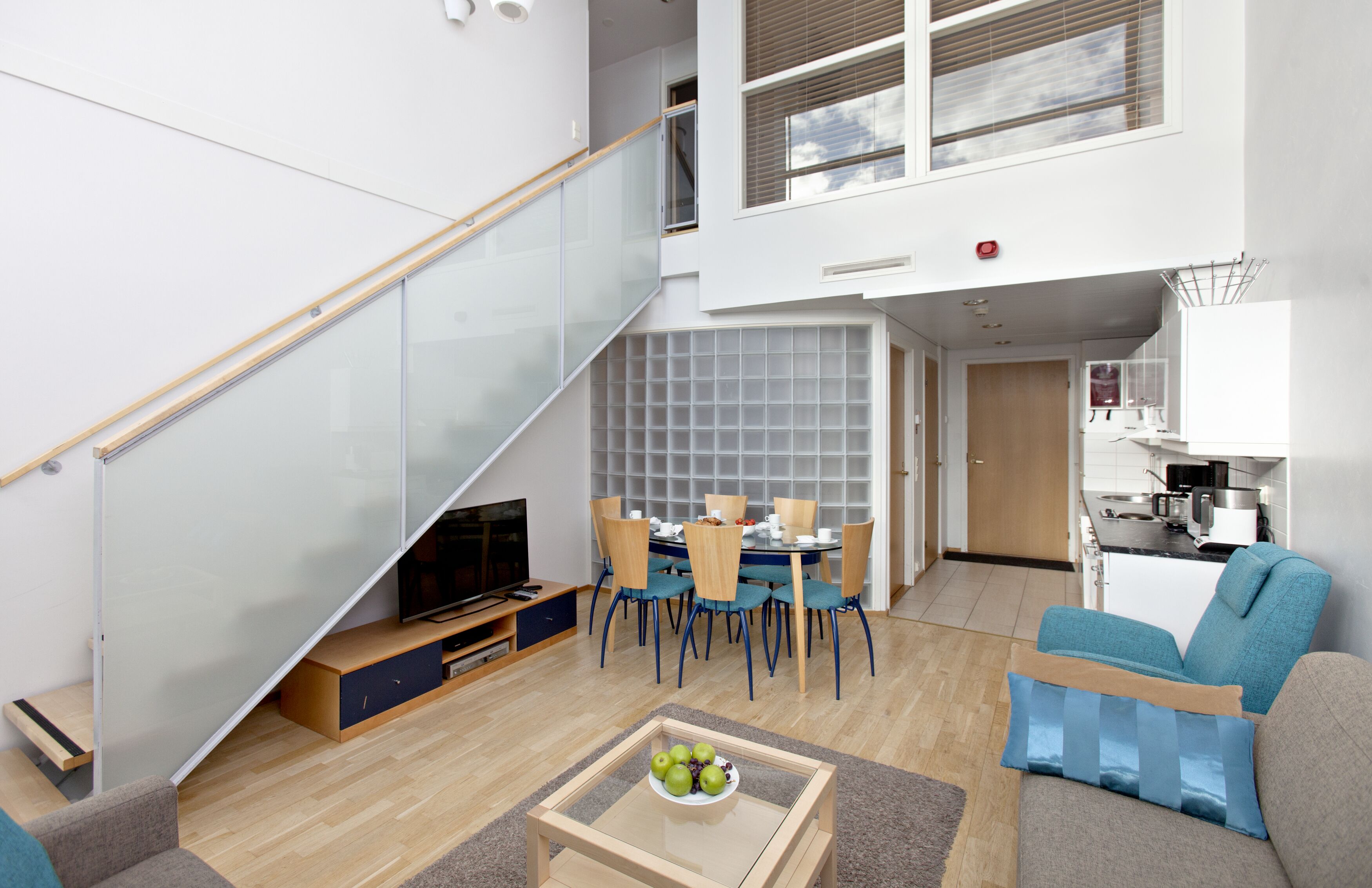 Una sala de estar moderna con una escalera de cristal, un comedor y una cocina.