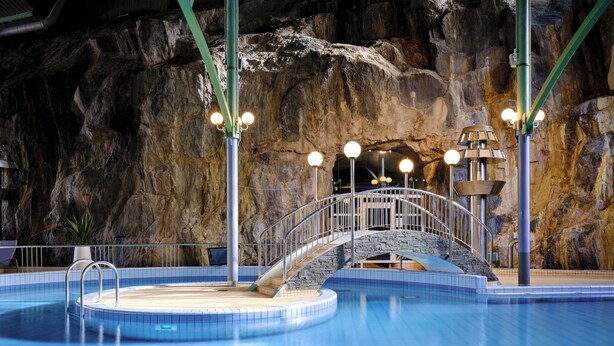 Uma piscina com uma ponte de pedra, grades de metal e um deck revestido com azulejos.
