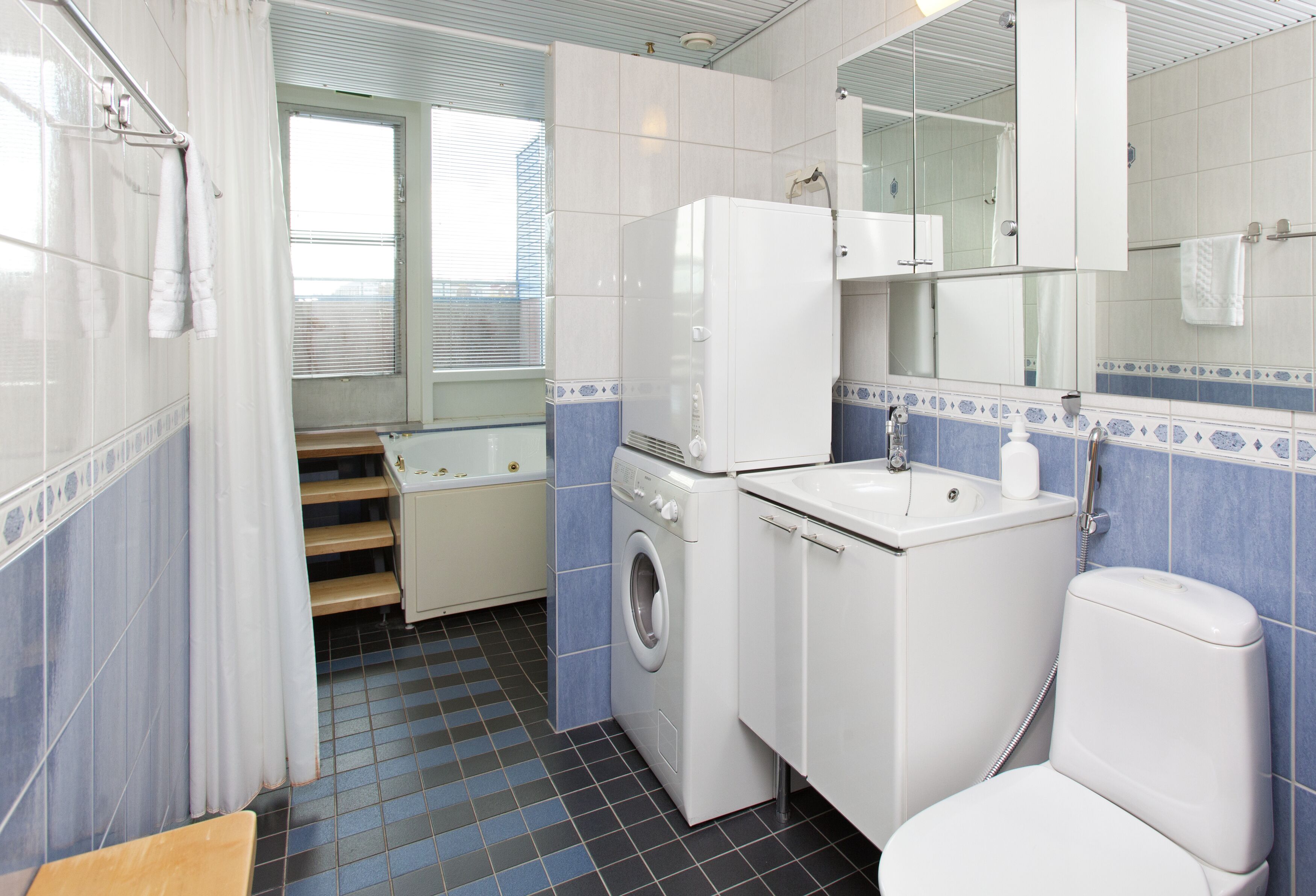 Baño compacto con lavadora, lavamanos e inodoro.