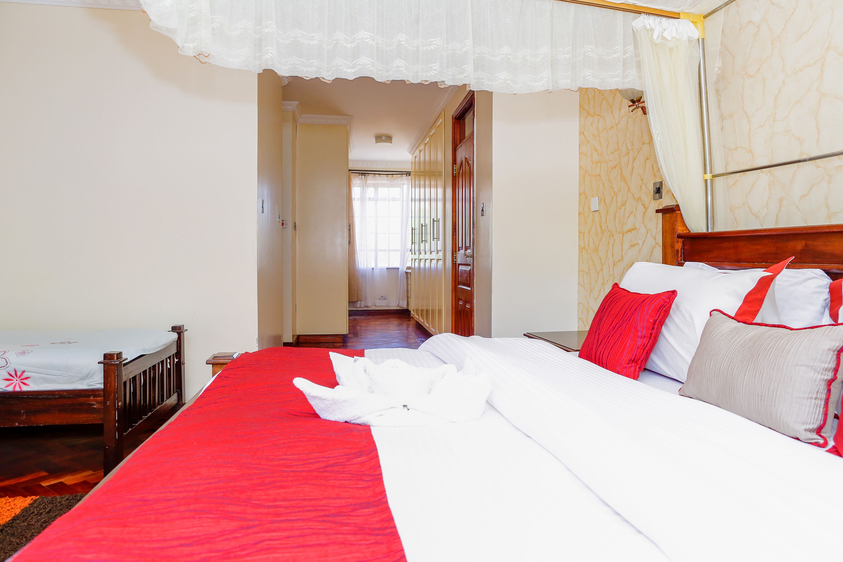 A hotel room with a large bed, a wooden headboard, and a red bedspread.