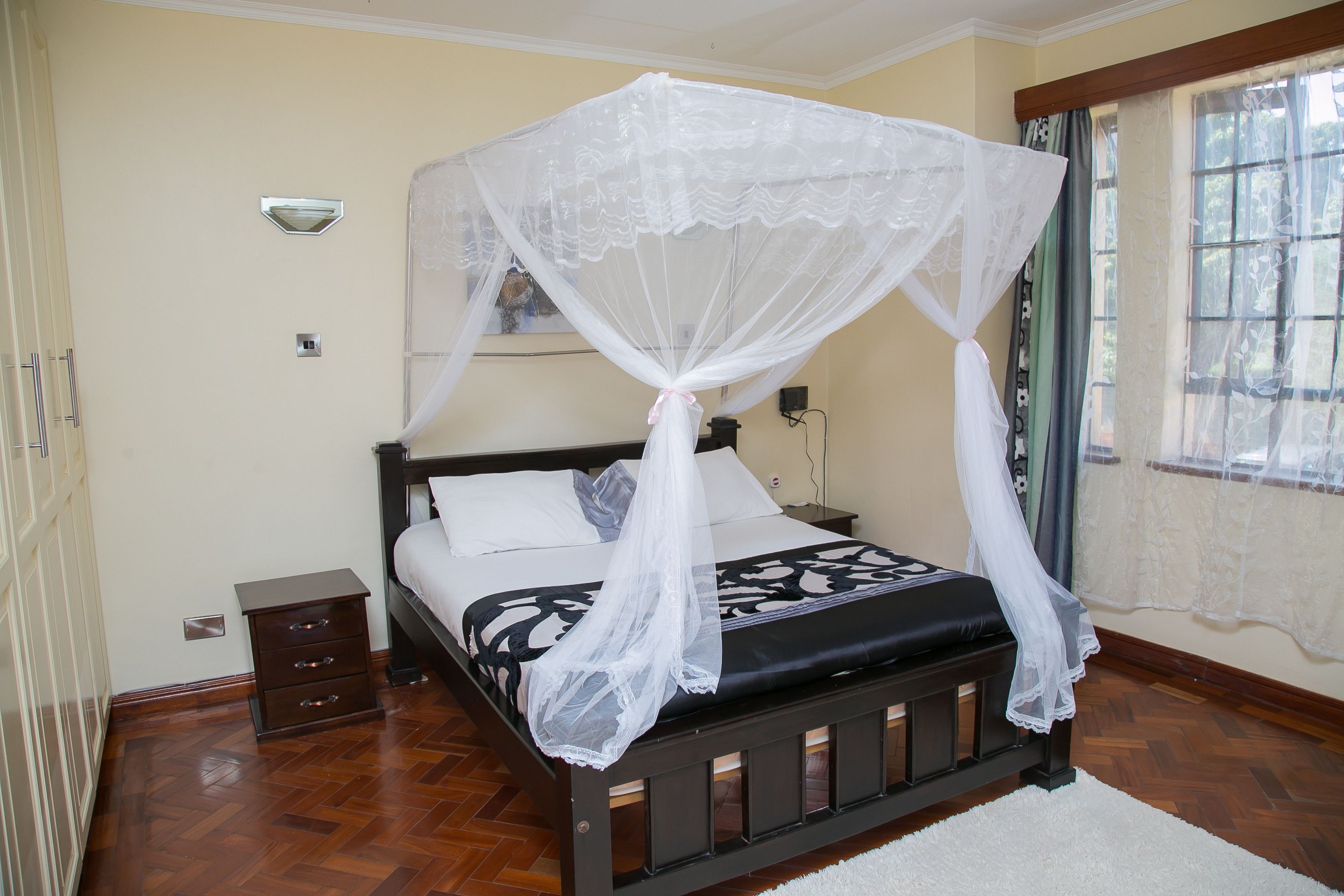 A bedroom with a bed, a nightstand, a drawer unit, and a window with curtains.