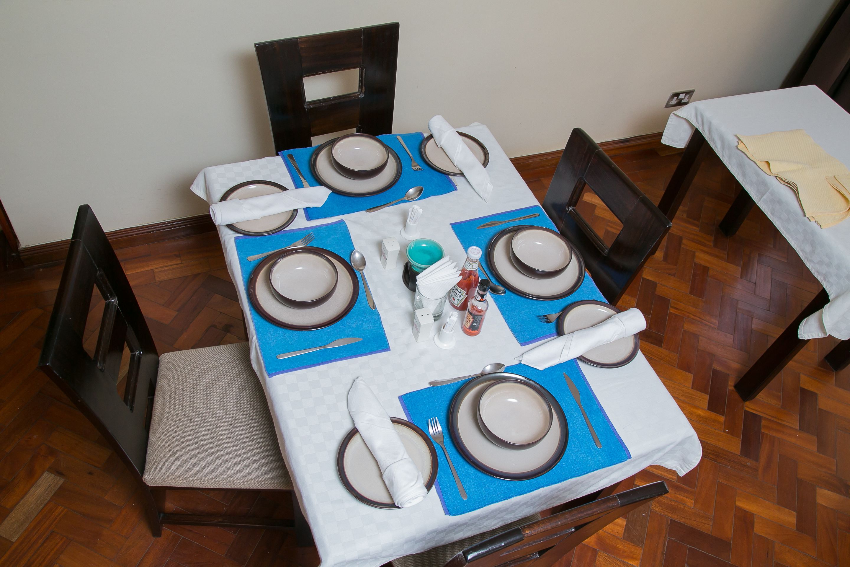 Une table à manger dressée avec des sets de table bleus, une nappe blanche et des assiettes marron.
