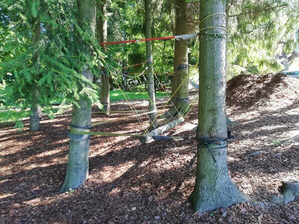 A rope bridge in a wooded area with trees and mulch on the ground.
