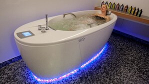Ett stort, modernt badkar med en kontrollpanel och LED-lampor, omgivet av ett golv med mosaikplattor.