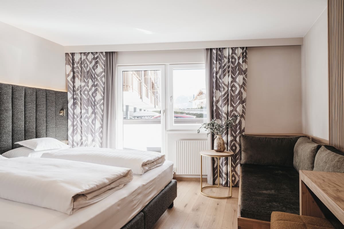 Une chambre d’hôtel avec un lit, un canapé, une petite table et une fenêtre avec des rideaux.