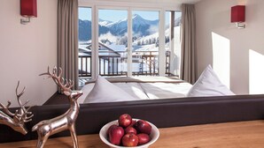 A hotel room with a bed, a view of mountains, a balcony, and a table with apples and a deer sculpture. - Hotel Chesa Monte (Fiss)