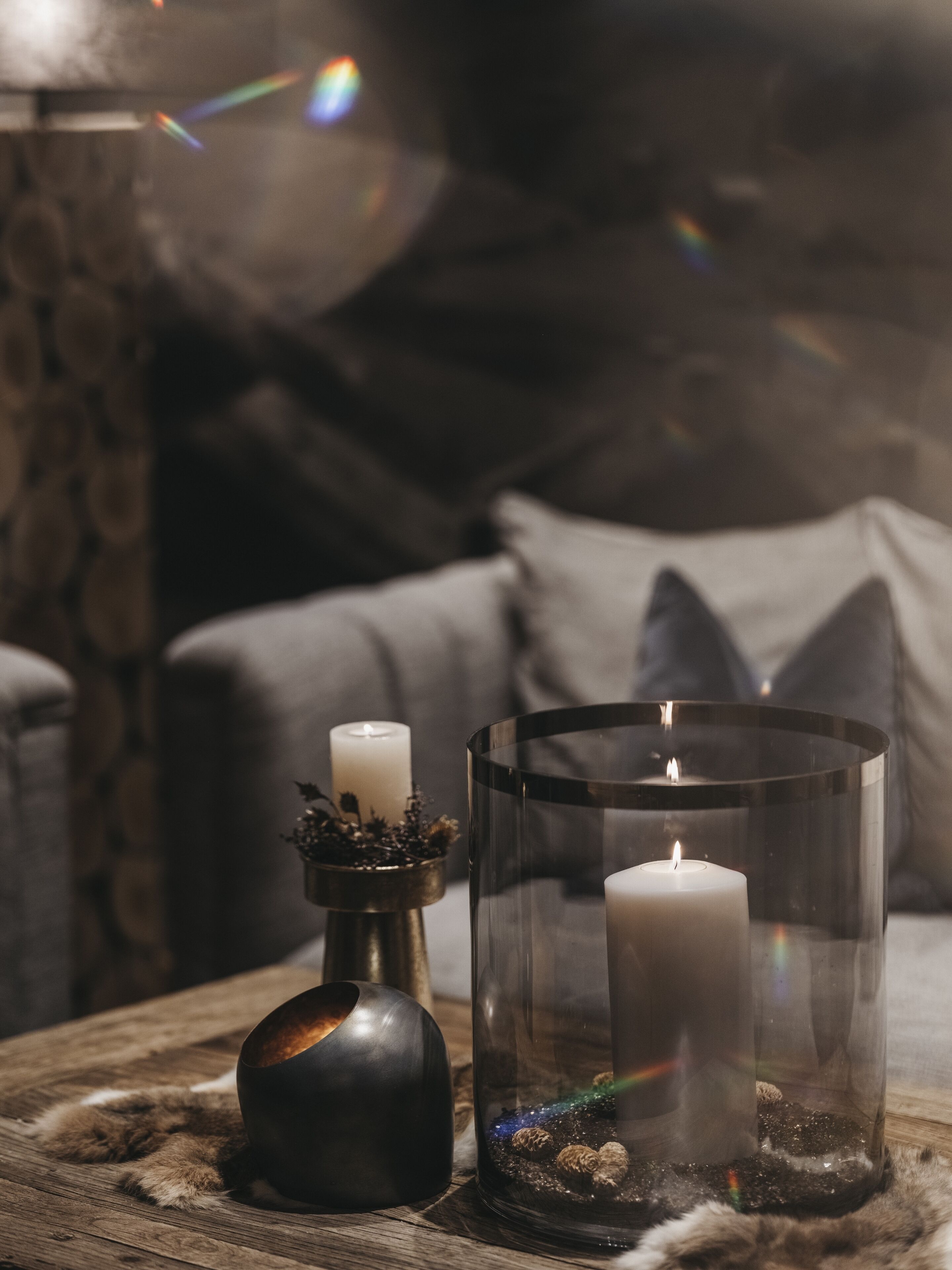 A candle in a glass holder on a wooden surface, with a lit candle in a glass container beside it.