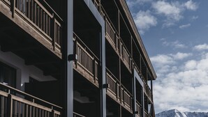A multi-story building with balconies and a mountainous backdrop. - Hotel Chesa Monte (Fiss)
