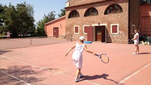 A tennis court with a brick building in the background. - Bordeghina B&B in Farmhouse (Pontecchio Polesine)
