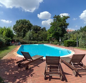 A rectangular swimming pool with a brick deck, surrounded by lush greenery and trees. - Bordeghina B&B in Farmhouse (Pontecchio Polesine)