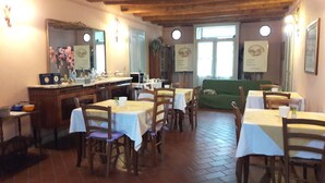 A restaurant with wooden tables and chairs, a counter with a cash register, and a green sofa. - Bordeghina B&B in Farmhouse (Pontecchio Polesine)
