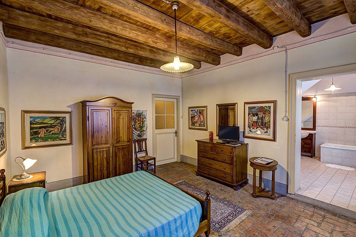 A bedroom with a bed, wooden wardrobe, television, and artwork on the walls.