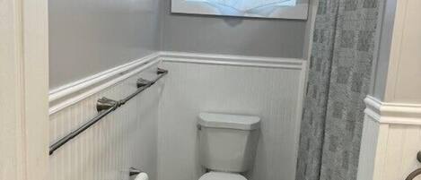 A small bathroom with a toilet, a window with a sheer curtain, and a shower curtain.
