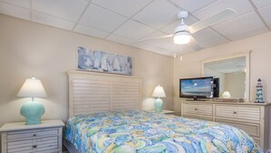 A bedroom with a bed, two bedside tables, a ceiling fan, a television, and a mirror. - Oceanfront condos with 3 night minimum rentals and linens included! (Ocean City)