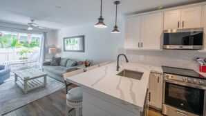 Une cuisine moderne avec des armoires blanches, un four en acier inoxydable et des luminaires suspendus.