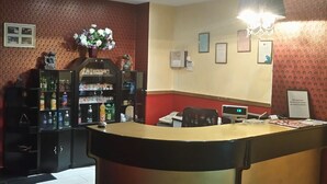 A reception area with a reception desk, a chandelier, a wall-mounted phone, framed certificates, and a vending machine.