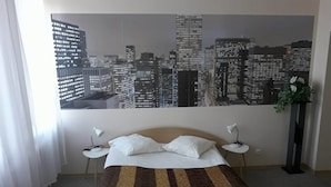 A hotel room with a bed, two bedside tables, a cityscape view, and a window with curtains.