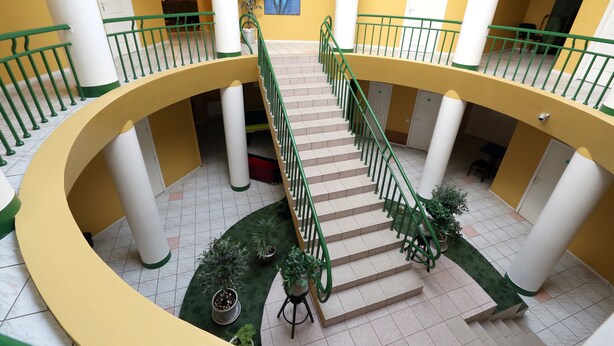 A multi-level interior with a central staircase, columns, and potted plants.