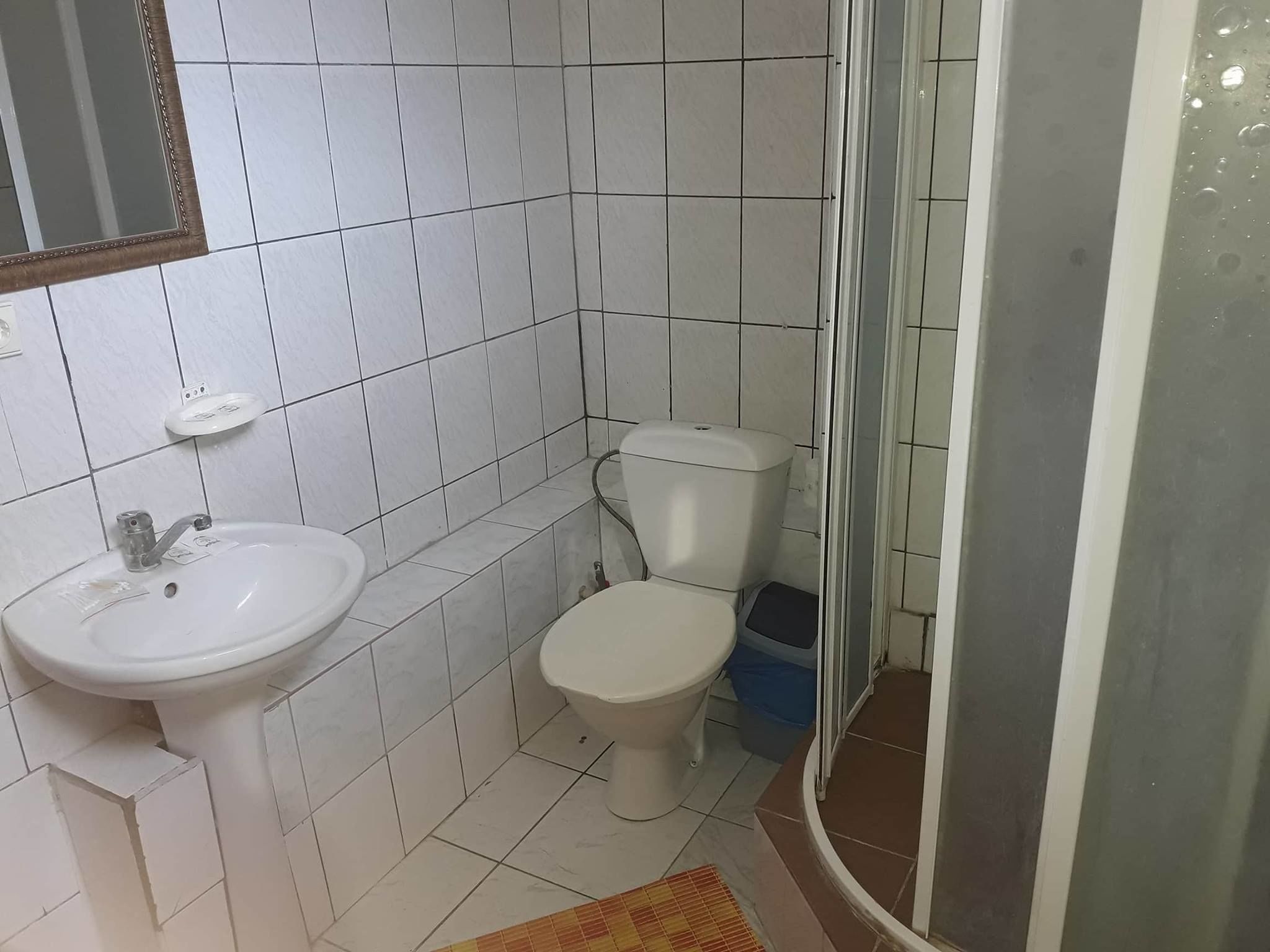 Kylpyhuone, jossa on valkoiset laatat, pesuallas, wc ja suihkutila.