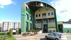 A hotel with a green and white facade, multiple windows, and a car parked in front.