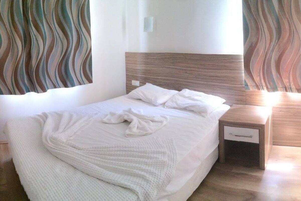 A bedroom with a bed, a bedside table, a nightstand, a mirror, and a window with curtains.