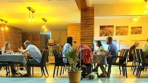 Un restaurant amb parets, taules i cadires de fusta, i llums penjants.