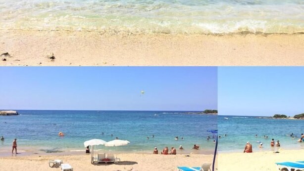 Una platja amb aigua cristal·lina, persones nedant i ombrel·les.