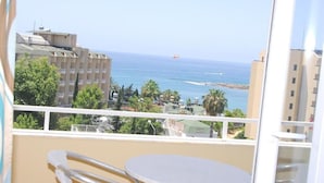 Un balcó amb taula i cadires, amb vista a una zona costanera amb edificis i al mar.