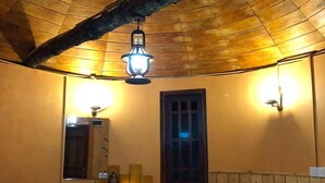 Una habitación acogedora con techo de madera, una cama con ropa de cama blanca y almohadas naranjas, una mesita de noche con una lámpara, y una ventana con vistas.