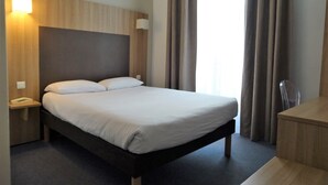 A hotel room with a bed, bedside table, lamp, and a desk with a chair. - Hôtel Saint Patrick Cœur de NANTES (Nantes)