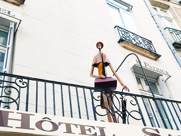 Un hotel llamado "Hôtel de la S." con barandilla de balcón y una estatua de una mujer.