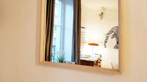 A room with a large mirror, a window with curtains, a lamp, and a wall with a decorative item. - Hôtel Saint Patrick Cœur de NANTES (Nantes)