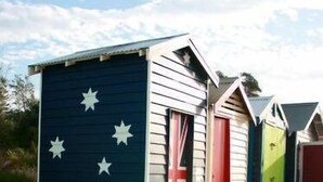 Eine Reihe von Strandhäusern mit australischen Flaggenmotiven, jedes mit einer kleinen Veranda.