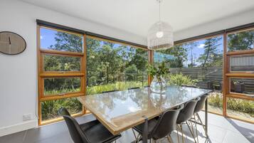 A modern dining area with a glass table, black chairs, and a view of the outdoors through large windows.