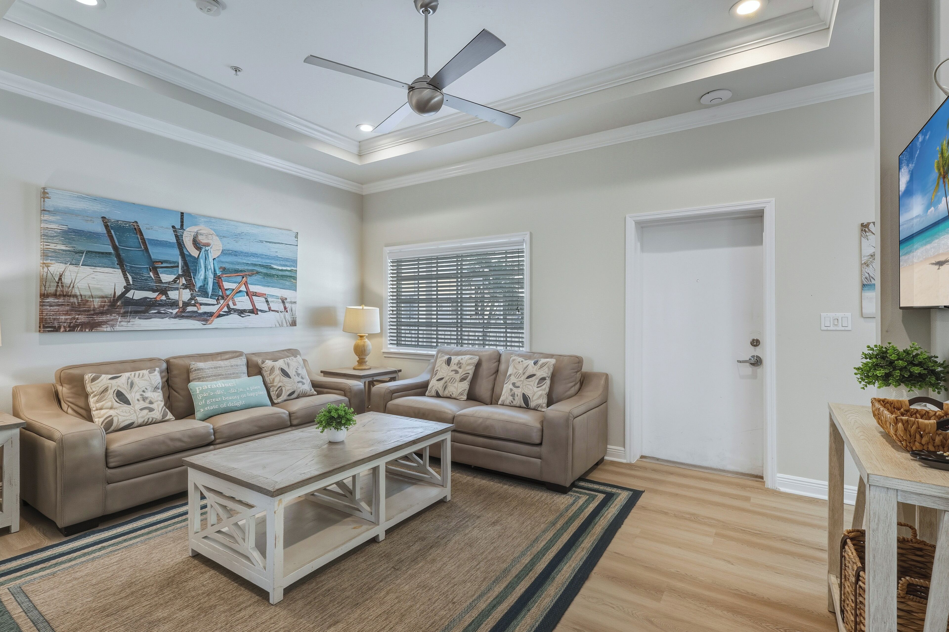 A living room with a beige sofa, a coffee table, and a painting of beach chairs.