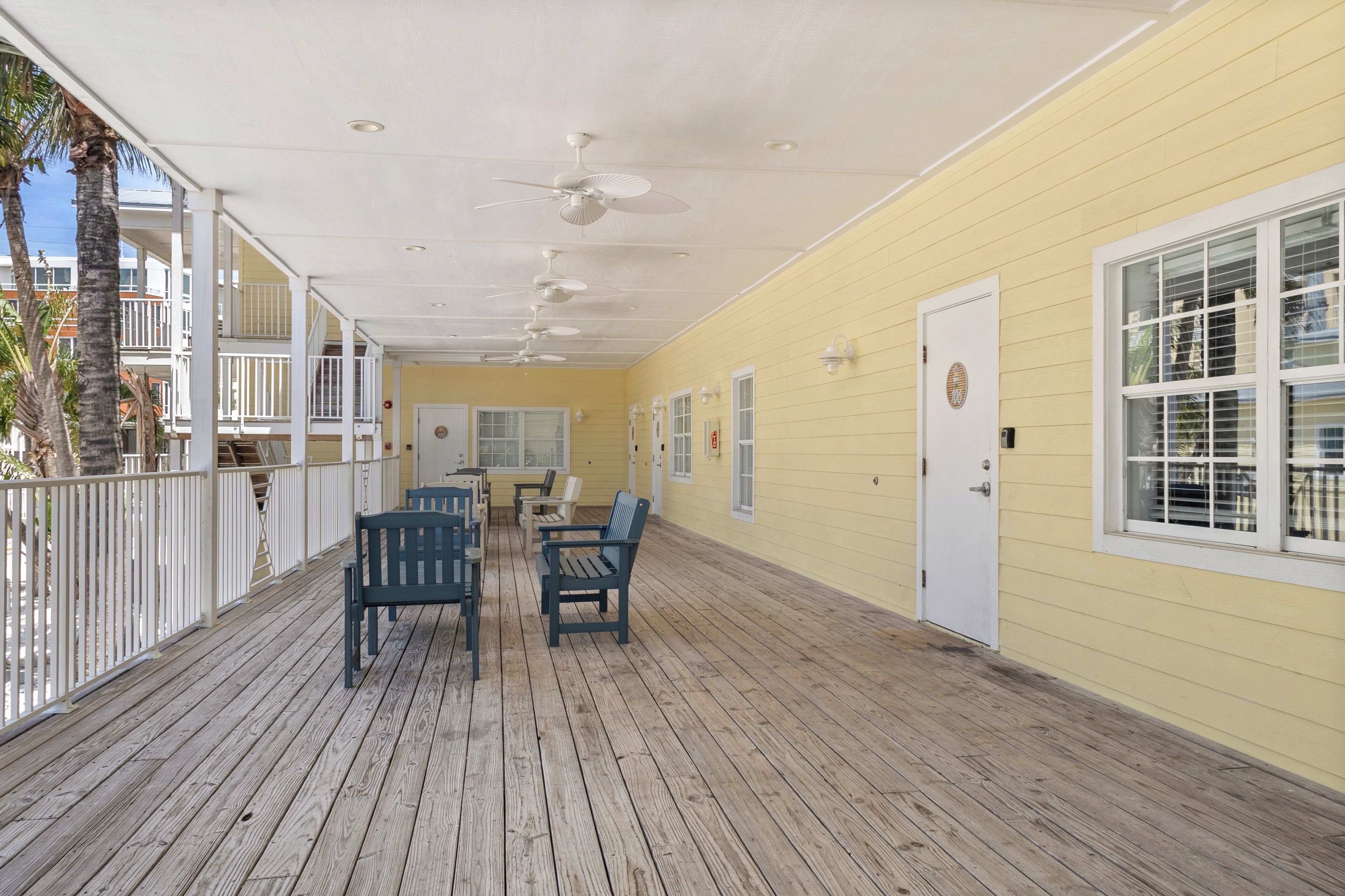 A covered outdoor area with wooden flooring, white railings, and ceiling fans.