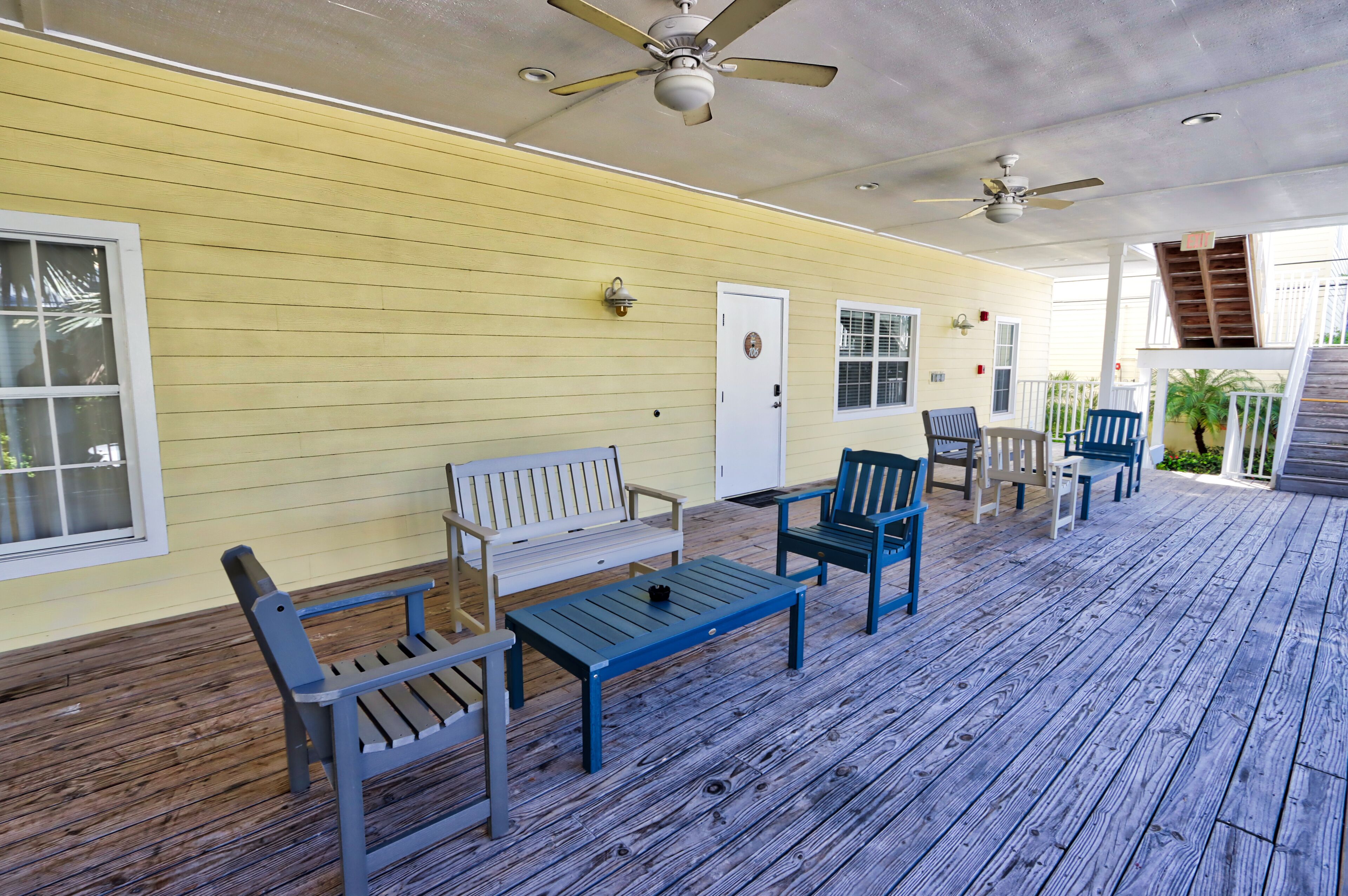 A covered outdoor area with wooden flooring, a white bench, and several chairs.