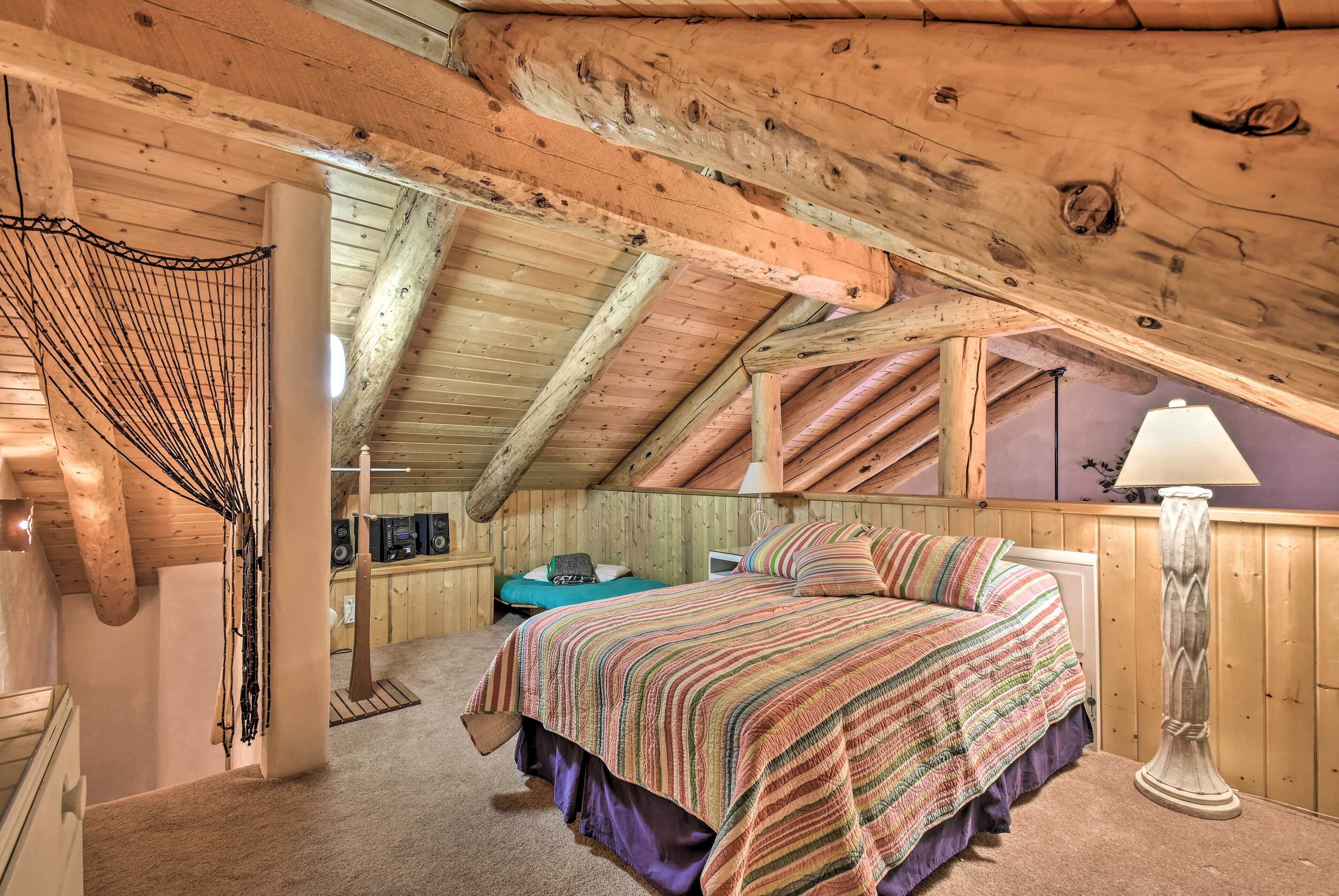Un dormitorio acogedor en el ático con techo inclinado de madera, una cama con colcha a rayas de colores y un pequeño escritorio con lámpara.