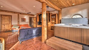 Een ruime kamer met een houten plafond, een bubbelbad en een gezellige zithoek met een bank en kussens.