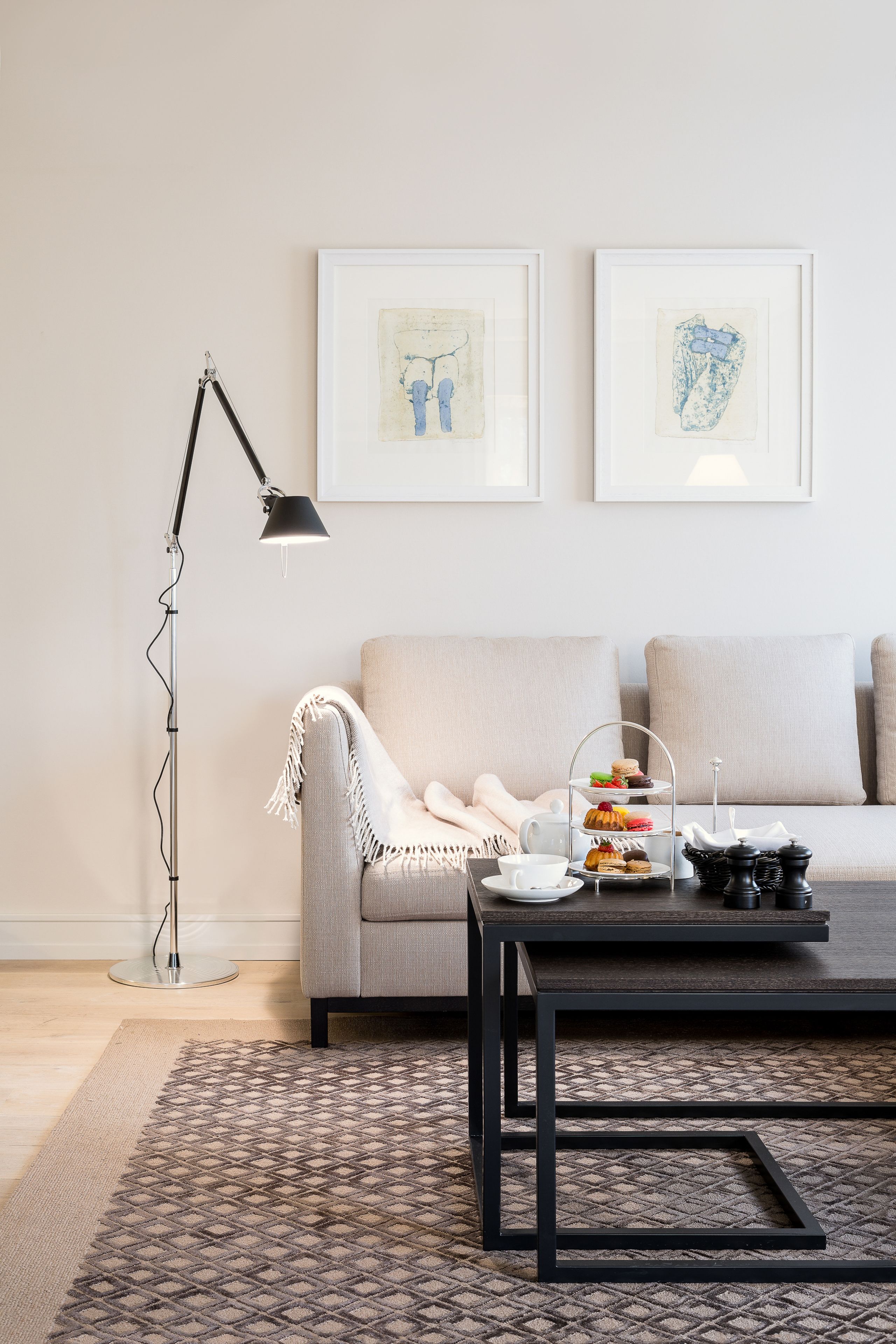 A modern living room with a sofa, a coffee table with a tiered tray of snacks, a floor lamp, and framed artwork on the wall.