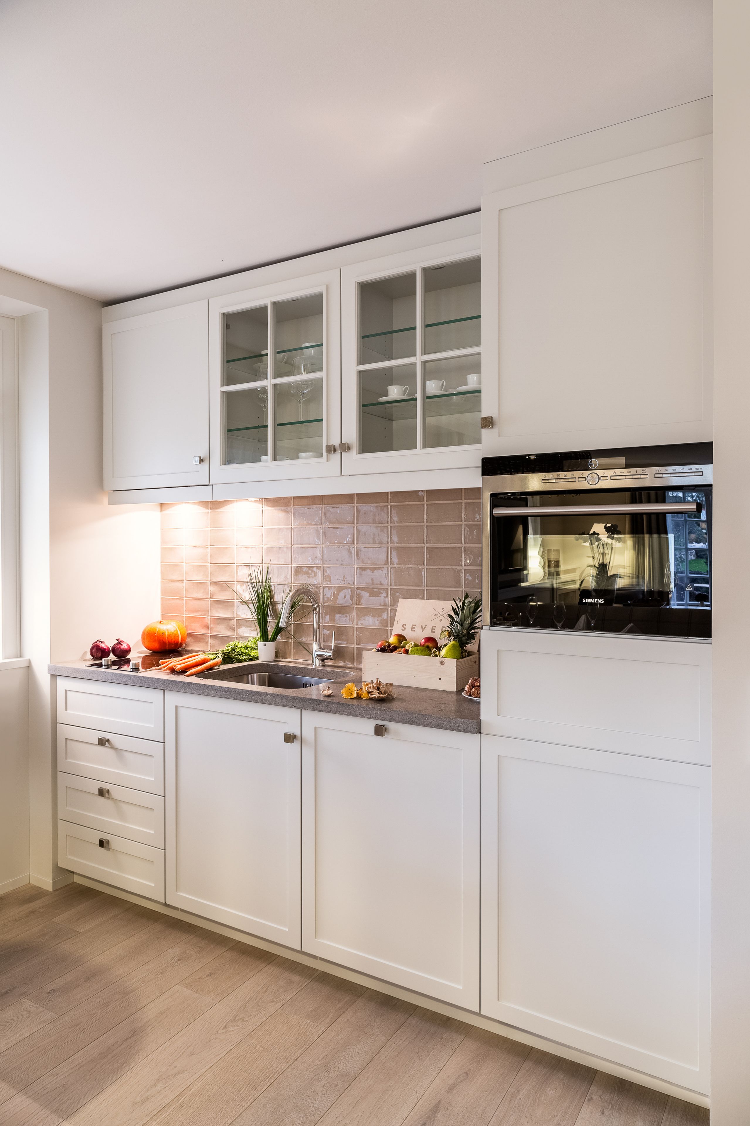 Una cocina moderna con armarios blancos, un lavaplatos de acero inoxidable y un horno empotrado.
