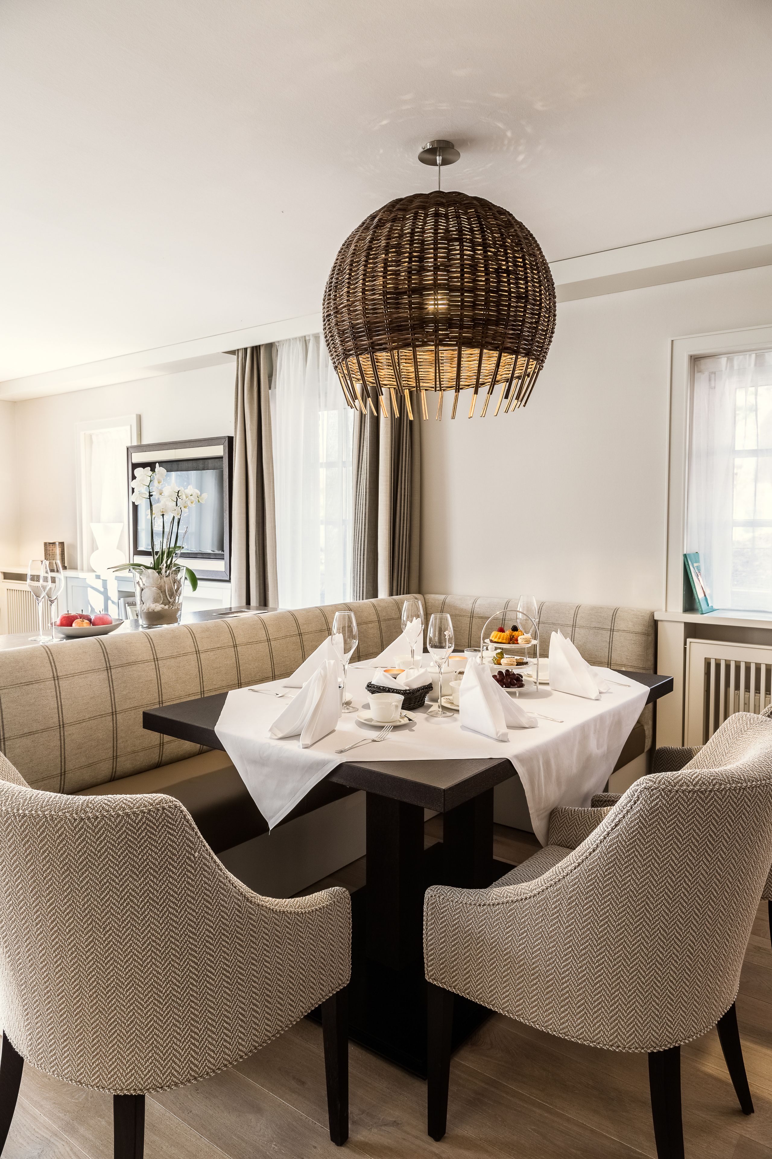A dining area with a round table, two chairs, a woven pendant light, and a sofa in the background.
