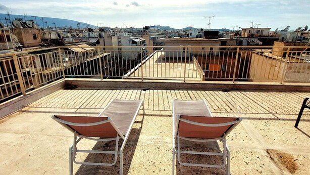 Terraza en la azotea con dos sillas de metal y barandilla metálica, con vistas a una zona urbana densamente poblada, con edificios y una montaña a lo lejos.