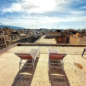 Terraza en la azotea con dos sillas de metal y barandilla metálica, con vistas a una zona urbana densamente poblada, con edificios y una montaña a lo lejos.