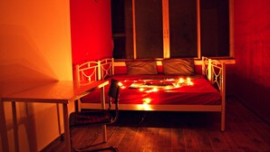 Una cama individual con una colcha roja y luces de hadas, un escritorio de madera y una silla en una habitación con paredes rojas y una ventana.