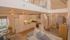 Een ruime loft met een keuken, eethoek en een trap naar een hoger gelegen niveau.
