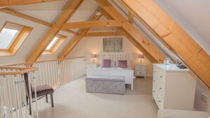 Een zolderkamer met hoge plafonds en een schuine kap, een bed met hoofdeinde, een nachtkastje, een dressoir en een raam.